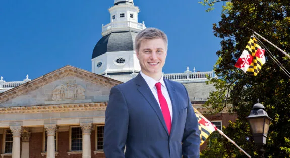 Smiling man in suit in front of a historic building with flags.