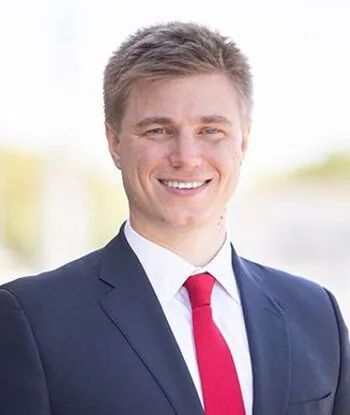 Smiling person in a suit with a red tie outdoors.